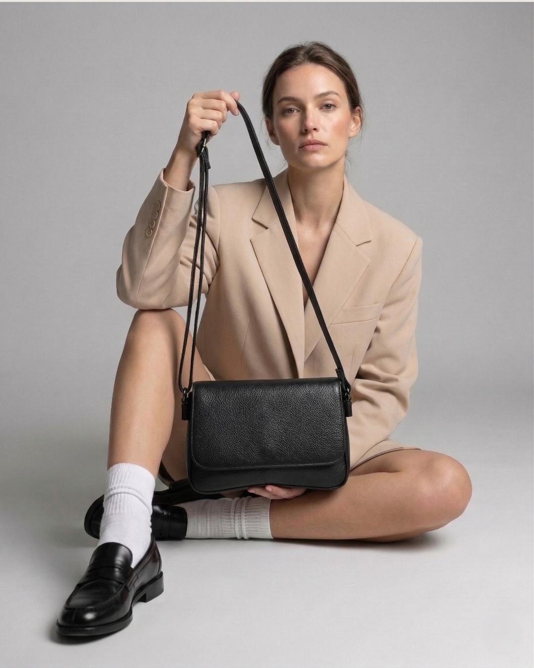 Woman holding a black handbag against a neutral background