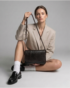 Woman holding a brown handbag against a plain background