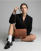 Woman holding a Tan leather bag against a gray background