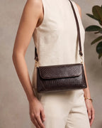 Woman carrying a brown croc-embossed shoulder bag with gold hardware and modern elegant style
