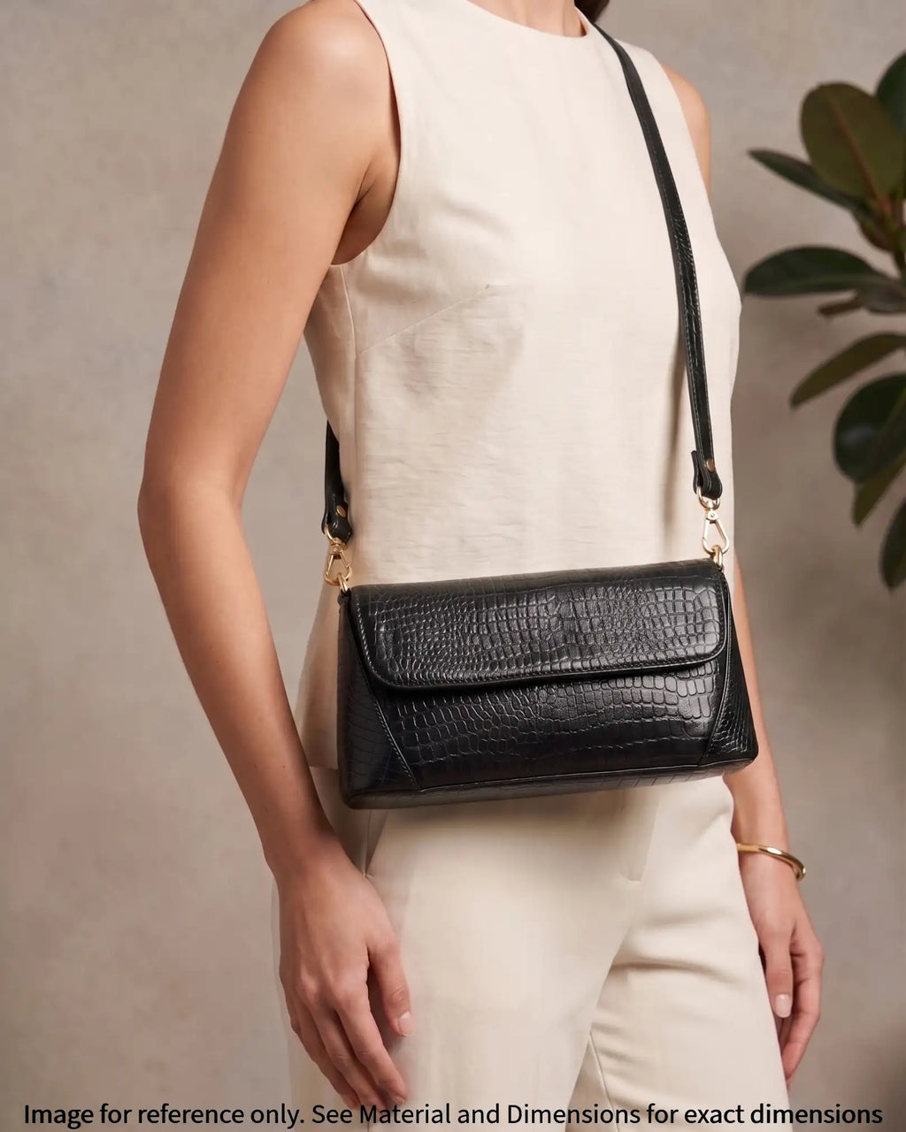 Woman carrying a black croc-embossed shoulder bag with gold hardware and modern elegant style