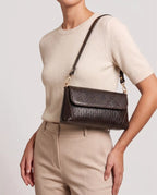 Woman carrying a brown croc-embossed shoulder bag with gold hardware and modern elegant style