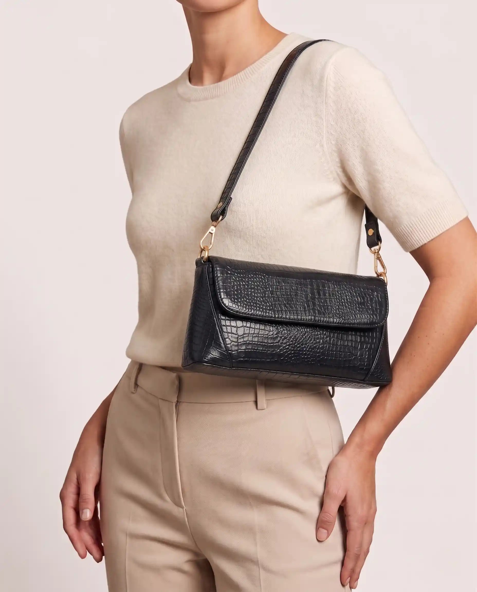 Woman carrying a black croc-embossed shoulder bag with gold hardware and modern elegant style